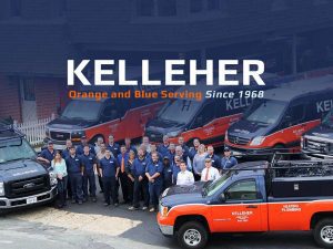 The Kelleher team standing for group photo, surrounded by branded blue and orange work vehicles.