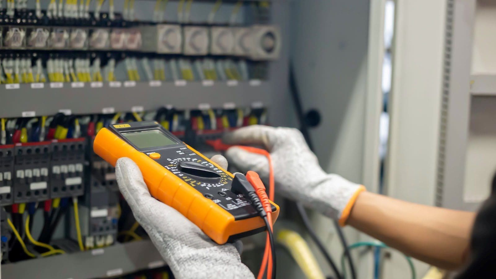 Electrician uses a multimeter to test the electrical installation and power line current in an electrical system control cabinet.