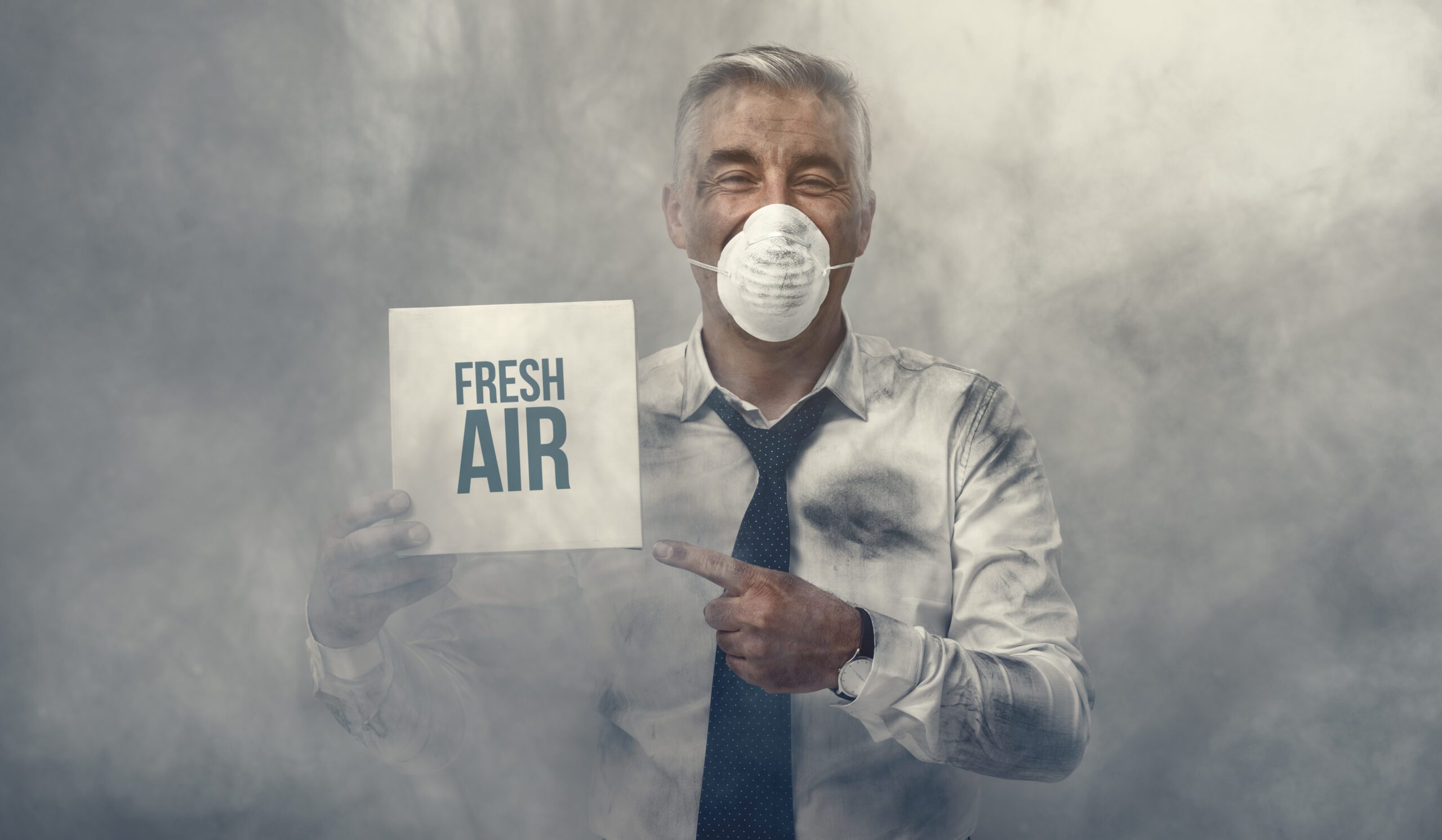 Man wearing mask, standing in smog, holding sign that says ‘fresh air’