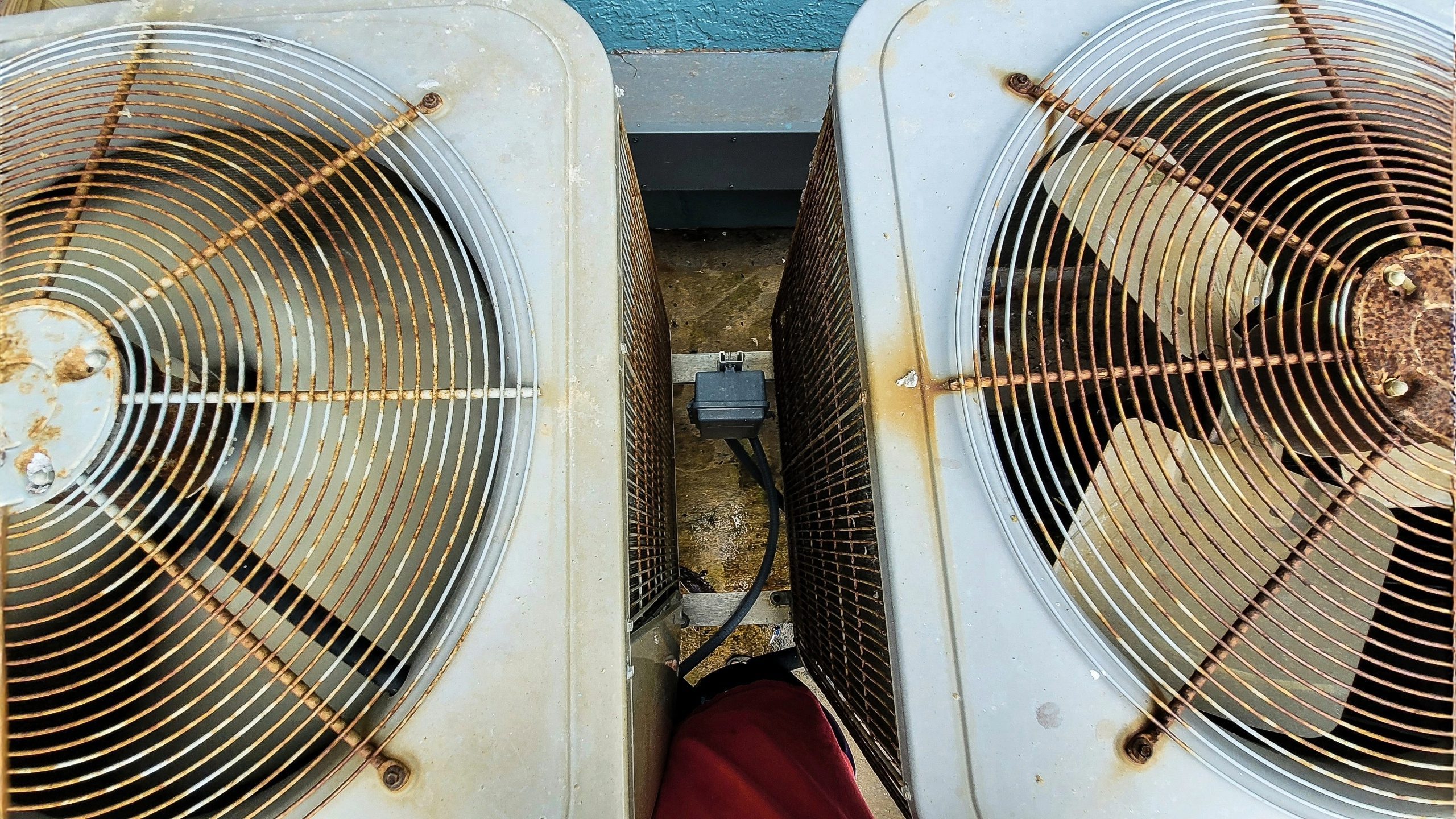 Time for HVAC replacement - Top-down view of two old and rusted outdoor HVAC condenser units installed side by side on a concrete slab, showing significant corrosion on fan grilles and housings